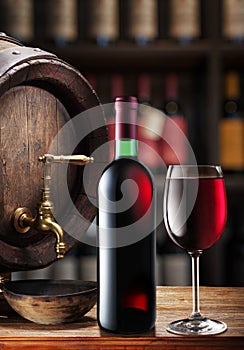 Wine bottle and glass of red wine on wooden cask. Wine shelves at the background