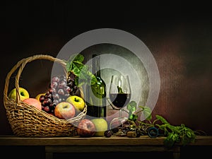 Wine bottle with glasses and basket of red grapes and apple on wooden table and background