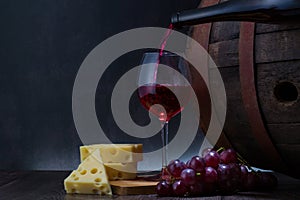 Wine bottle, grapes, cheese, glass of red wine and old wooden barrel