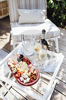 Wine bottle mockup with blank stickers. Ice cooler, two glasses of champagne and plate of delicious dessert on glass table