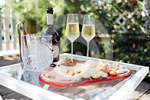 Wine bottle mockup with blank stickers. Ice cooler, two glasses of champagne and plate of delicious dessert on glass table