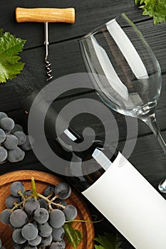 Wine bottle and wine glass with grapes on black wooden background. Vertical photo