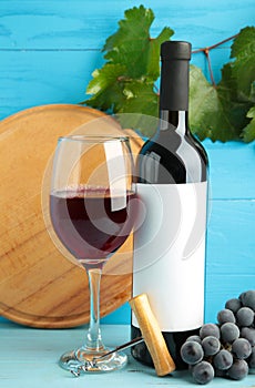 Wine bottle and wine glass with grapes on blue wooden background. Vertical photo