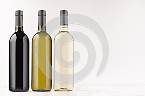 Wine bottles collection different colors - transparent, green, black- on white wooden board, mock up, copy space.