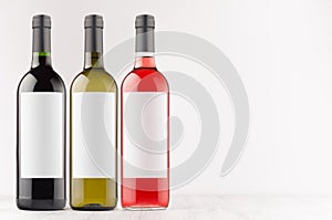 Wine bottles collection - red, green, black- with blank white labels on white wooden board, mock up, copy space.