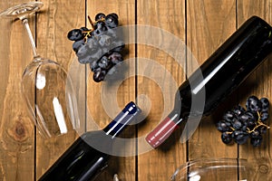 Wine bottles glass cups and grape bunches on wooden background. Top view with copy space