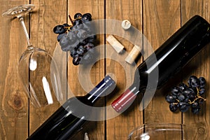 Wine bottles glass cups and grape bunches on wooden background. Top view with copy space