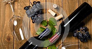 Wine bottles glass cups and grape bunches on wooden background. Top view with copy space