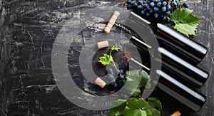 Wine bottles, grapes, grape bunches with leaves and vines corkscrew wine corks on dark rustic concrete background. Flat lay wine