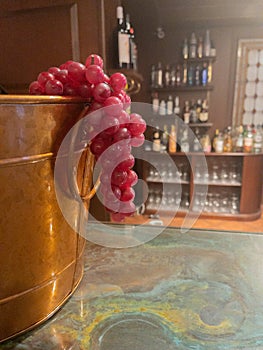 Wine bucket with bunch of red grapes hanging with bottles in the background