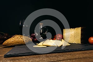 Wine, cheese, bread, tomatoes on a board on a black background