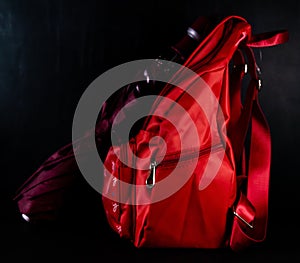 A wine colored umbrella with a red school bag shot against black board haing stains of white chalk -monsoon and schools concept