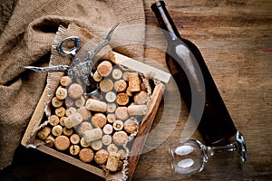 Wine corks of different sizes, a corkscrew, a bottle of wine and a glass shot on an old wooden surface. Background for liquor