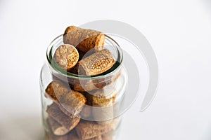 Wine corks lie in a glass jar on a white background