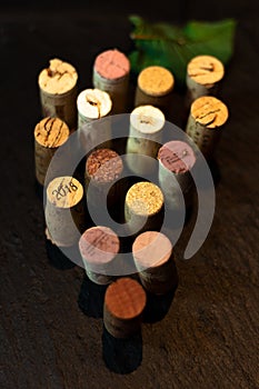 Wine corks placed forming a bunch of grapes and a grape leaf over a slate with dark background