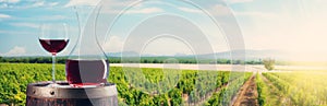 Wine decanter and glass on wine barrel in front of vineyard