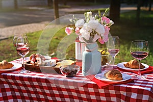 Wine, food and flowers on picnic table on sunny day