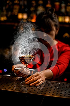 wine glass with brown drink stands on bar counter and female bartender sprinkles over it