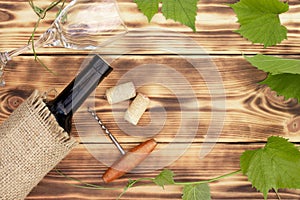 Wine glass, corkscrew, corks, wine bottles, grapevine on rustic burnt wooden background. Top view. Copy space