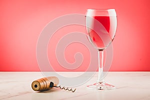 Wine glass and corkscrew on pink background/Wine glass and wooden corkscrew on pink background. Selective focus