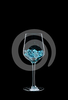 Wine glass filled with transparent blue crystals backlit and isolated on black background.
