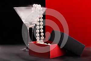 Wine glass with fog and perl beads falling into opened paper giftbox on foggy glossy surface