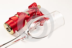 Wine glass in the foreground against the background of a bottle of champagne wrapped with a red silk ribbon on a white background