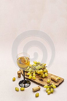 Wine glass, fresh grapes and corks on wooden chopping board. Wine bar, winery, wine tasting concept. Stone concrete background photo