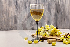 Wine glass, fresh grapes and corks on wooden chopping board. Wine bar, winery, wine tasting concept. Stone concrete background photo