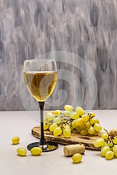 Wine glass, fresh grapes and corks on wooden chopping board. Wine bar, winery, wine tasting concept. Stone concrete background photo