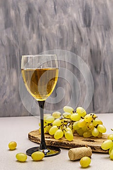 Wine glass, fresh grapes and corks on wooden chopping board. Wine bar, winery, wine tasting concept. Stone concrete background photo