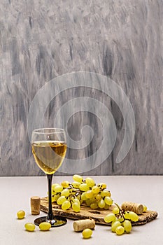 Wine glass, fresh grapes and corks on wooden chopping board. Wine bar, winery, wine tasting concept. Stone concrete background