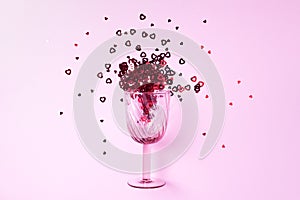 Wine glass with heart confetti on pink background. Top view. Valentines day and romantic love concept. Copy space