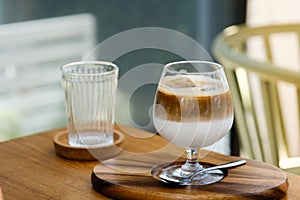 Wine glass of iced coffee two layers fresh milk and espresso short on wooden table at cafe. Refreshing summer drink concept.