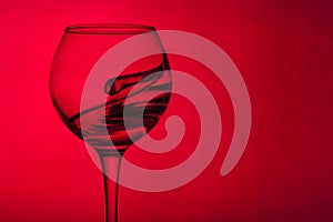 Wine glass with liquid on a red background. The liquid in the glass splashes.