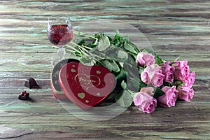 Wine in a glass, roses and a box of chocolates on a wooden table