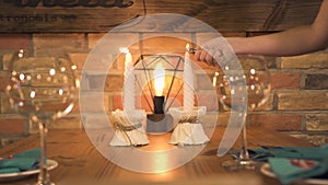 Wine glass standing on served dinner table with burning candle for romantic date in restaurant. Waitress lighting candle
