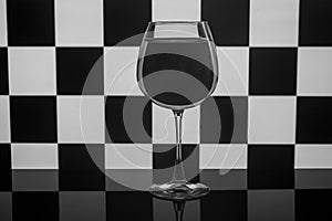 A wine glass stands on a chessboard background.