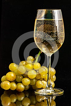 Wine glass with wine and a bunch of grapes against a black background