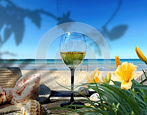 Wine glass and women hat on wooden bench on beach blue sky white sand yellow flowers  shadow green sea water summer holiday