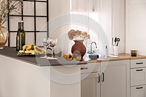 Wine, glasses and fruits on marble kitchen counter in elegant interior with white cupboards