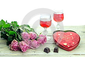 Wine in glasses, roses and a box of sweets on a wooden table