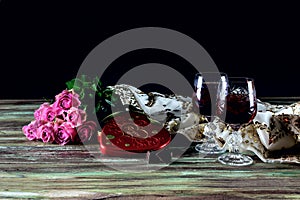 Wine in glasses, roses and a box of sweets on a wooden table