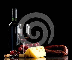 Wine, grapes, cheese and sausage on black background