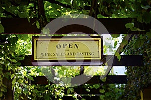 Wine sales and tasting signs at quaint winery entrance covered in grapevines.