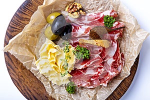 Wine set: dried neck, cheese, olives and rye crackers. Seth is lying on crumpled parchment paper on a round wooden tray.