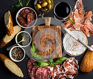 Wine snack set with empty wooden board in center. Glass of red, meat selection, mediterranean olives, sun-dried tomatoes