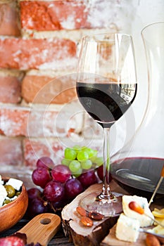 Wine snack set. Glass of red wine, grape and various sorts cheese, over rustic wooden background.