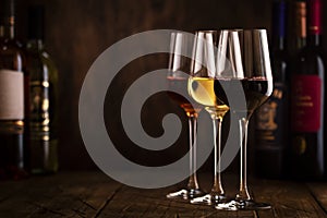 Wine tasting. Red, white and rose wine in glasses on wooden background in rustic cellar or bar with collection of wine bottles,