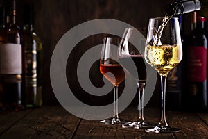 Wine tasting. White wine pouring into glass on background with selection of red, white and rose wines in glasses and bottles